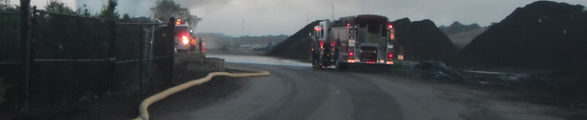 A smoky brush fire is shown with two trucks facing away.