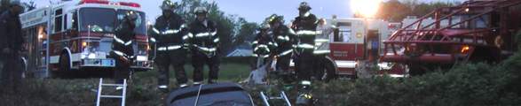 A group of firefighters stand around a car in a ditch.